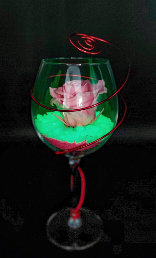 Rosa rosa preservada en la copa de cristal. La piedra que adornada la rosa se ilumina en oscuridad.